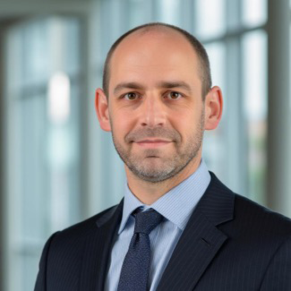 Portrait of Pascal Cornuez in a dark suit and tie with a blurred office background.